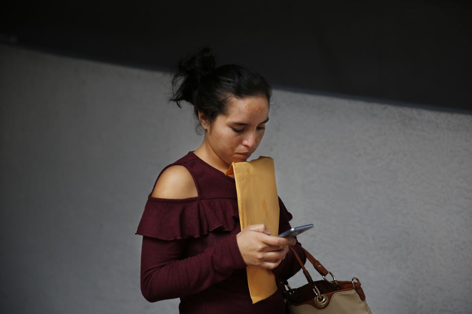 Dania Rivas, 20, of Honduras, clutches an envelope while looking at her phone outside of immigration court after court hearings were canceled on Thursday, Jan. 31, 2019, in Miami. U.S. immigration officials blame the government shutdown and the extreme winter weather for confusion about immigration court hearings. In an emailed statement, the part of the Justice Department overseeing immigration courts said some immigrants with notices to appear Thursday wouldn't be able to proceed with those hearings. (AP Photo/Brynn Anderson)