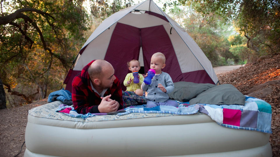 Father and children sitting on camping mattress outside tent