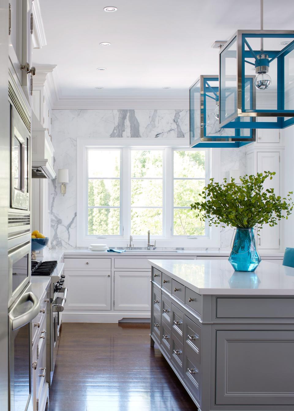 To enhance the natural light streaming into the kitchen, Hepfer painted the dark wood cabinets crisp shades of white and gray. A massive slab of Statuario Venato marble surrounds the windows on the wall above the sink.