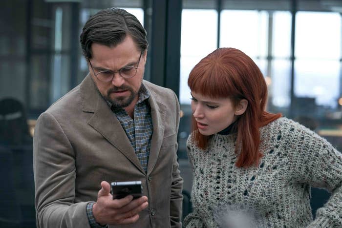 Leonardo DiCaprio's character looks down at a phone alongside Jennifer Lawrence's character