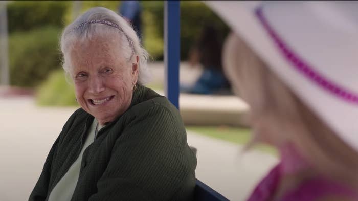 An older woman sitting on a bench, smiliing, as seen in 