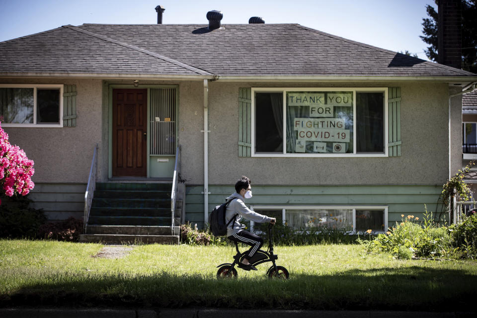 FILE - A man rides a small bicycle past a house with the message "Thank you for fighting COVID-19" hung in the window, in Vancouver, British Columbia, Monday, May 18, 2020. In 2019, nearly 9% of all trips in Vancouver were by bicycle, one of the highest rates measured in North America. After a decade of expansion, Vancouver offered about 270 km (168 miles) of safe, convenient and low-stress cycling routes on off-street bike paths, protected on-street lanes and local street bikeways, according to a Rutgers-Virginia Tech study of cycling in more than a dozen cities in North America and Europe. (Darryl Dyck/The Canadian Press via AP, File)