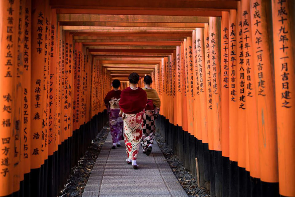 Three women in kimonos walk through the Fushimi Inari Shrine