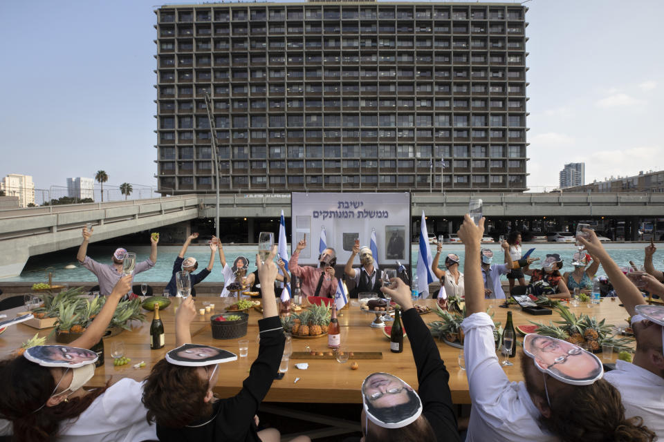 Israeli activists wear masks depicting Israeli Prime Minister Benjamin Netanyahu and other ministers during a mock cabinet meeting protesting the government's response to the health and economic crisis in Tel Aviv, Israel, Sunday, Sept. 6, 2020. Hebrew reads: "Detached government meeting" . (AP Photo/Sebastian Scheiner)