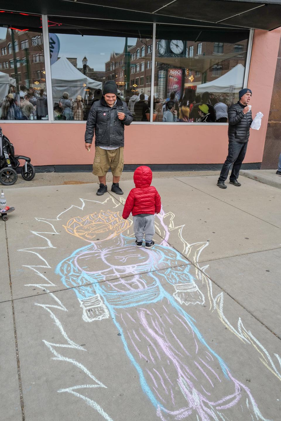 Chalk artist Don Martinez interacts with a child who likes walking on his handiwork at the East Lansing Art Festival Saturday, May 20, 2023.