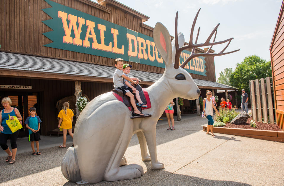 Kids on a statue of a jackalope in front of storefront that says "Wall Drug"