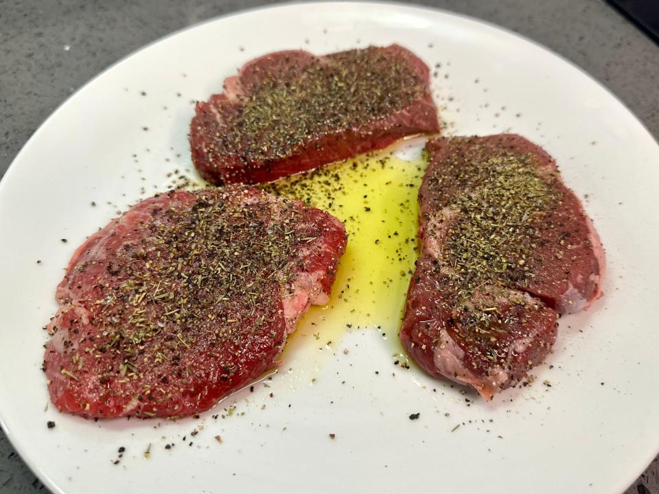 Three pieces of stake covered in olive oil and seasoning.