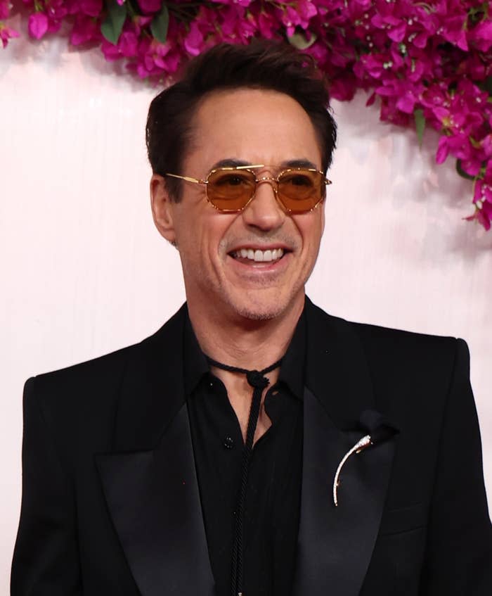 Man in a black suit and sunglasses smiling at a formal event