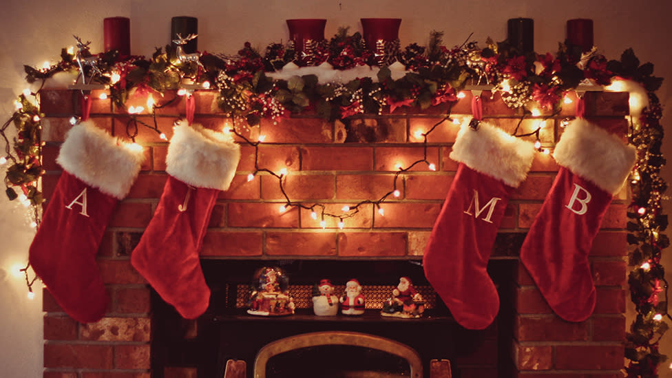 Red Christmas stockings hang above a fireplace with decorations on the mantle