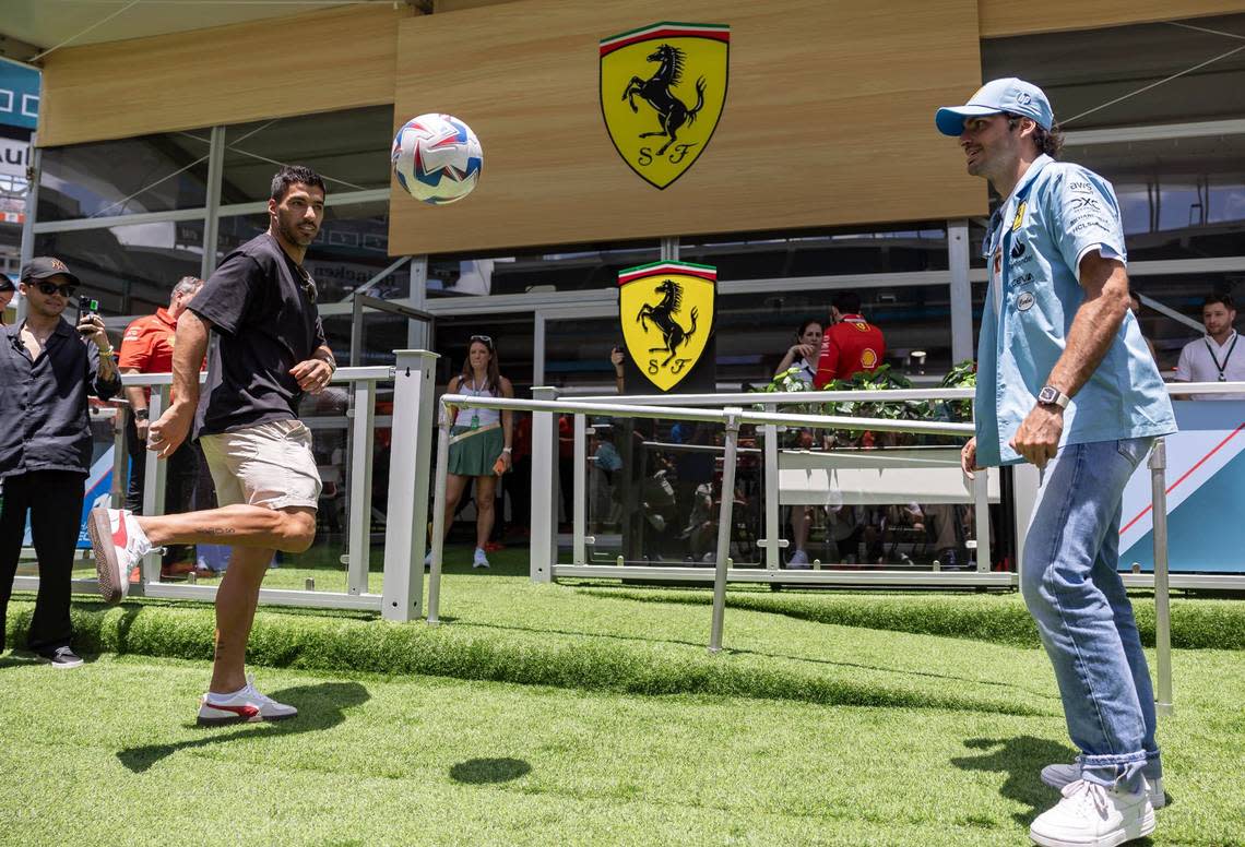 Inter Miami forward Luis Suarez, left and Scuderia Ferrari driver Carlos Sainz Jr., right, kick a soccer ball at the Team Village inside Hard Rock Stadium the first day of the Formula One Miami Grand Prix at the Miami International Autodrome in Miami Gardens, Florida