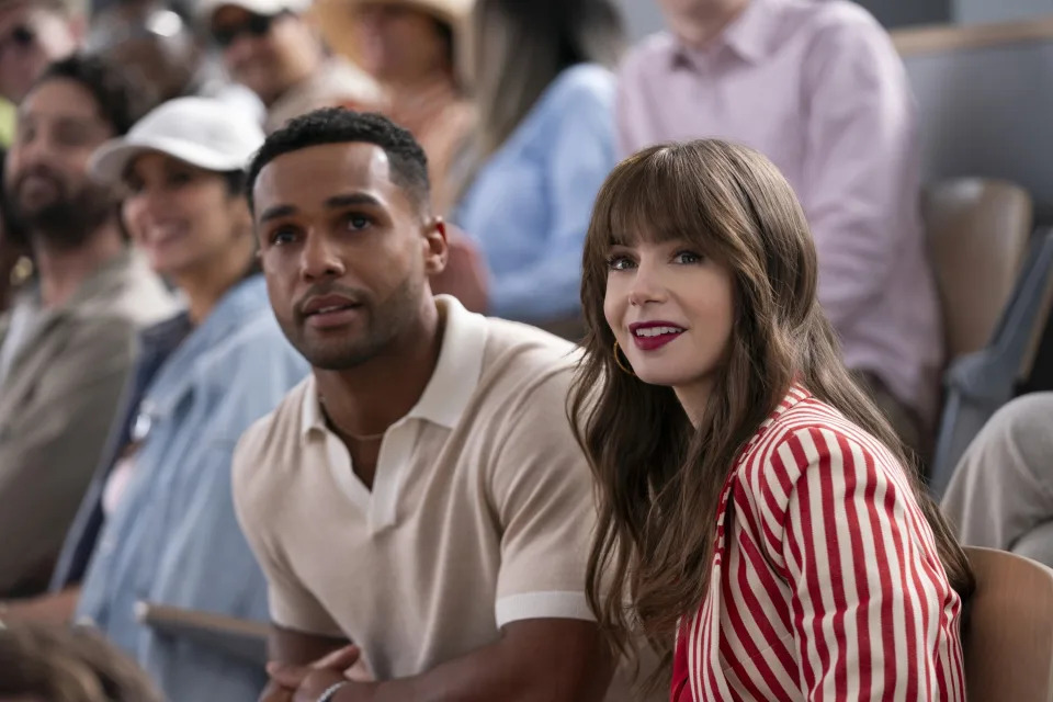 Lucien Laviscount and Lily Collins sitting in a crowd in "Emily in Paris"