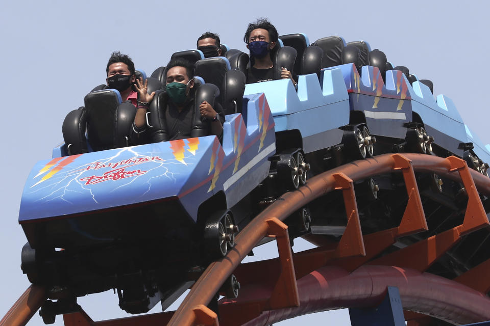 Indonesian men wearing protective masks sit spaced apart as they enjoy a ride at Dunia Fantasi Amusement Park during its first day of reopening after weeks of closure due to the large-scale restrictions imposed to help curb the new coronavirus outbreak, at Ancol Dream Park in Jakarta, Indonesia, Saturday, June 20, 2020. (AP Photo/Tatan Syuflana)