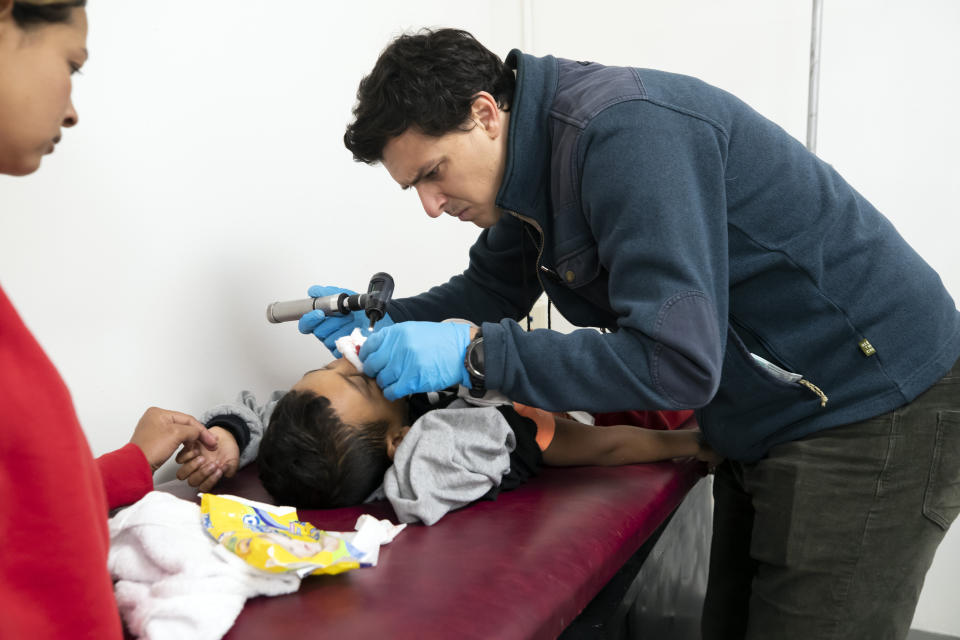 Dr. Brian Elmore, right, with the Texas Tech University Health Sciences Center in El Paso, Texas, checks the bleeding nose of Honduran migrant Elvin Cruz, 5, as his mother, Diana Rosales, looks on at a government-run shelter in Ciudad Juarez, Mexico, on Sunday, Dec. 18, 2022. (AP Photo/Andres Leighton)