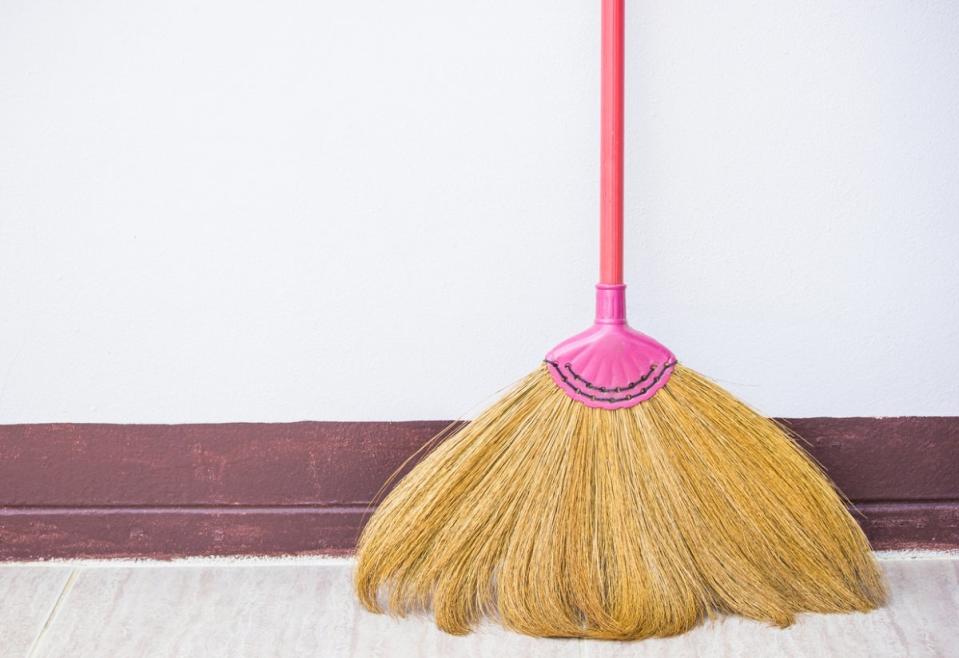 Old broom in home against a wall with painted baseboards