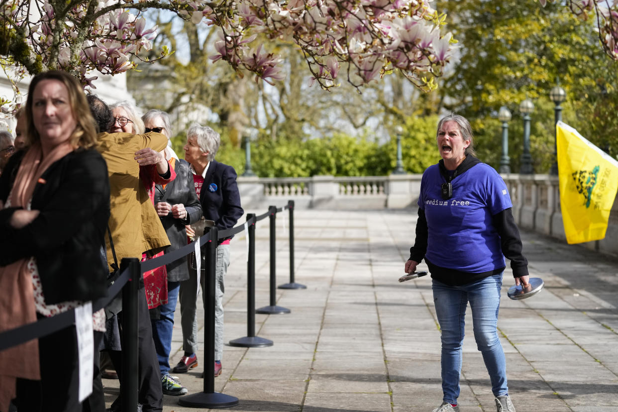 Sara Jones, right, with "We the People Against Communism," yells at guests lining up to enter the Capitol while she protests ahead of the signing of firearms regulation bills by Washington Gov. Jay Inslee, Tuesday, April 25, 2023, in Olympia, Wash. (AP Photo/Lindsey Wasson)