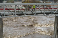 People cross a bridge over a swollen Los Angeles River in Los Angeles on Saturday, Jan. 14, 2023. Storm-battered California got more wind, rain and snow on Saturday, raising flooding concerns, causing power outages and making travel dangerous. (AP Photo/Damian Dovarganes)