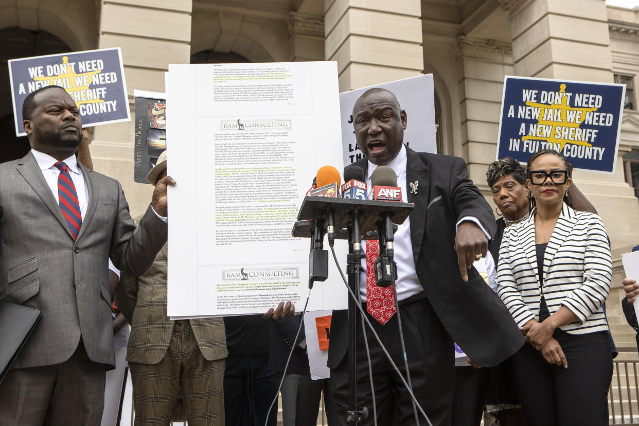 Attorney Ben Crump at the microphone, with people beside him holding posters saying: We don't need a new jail, we need a new sheriff of Fulton County.