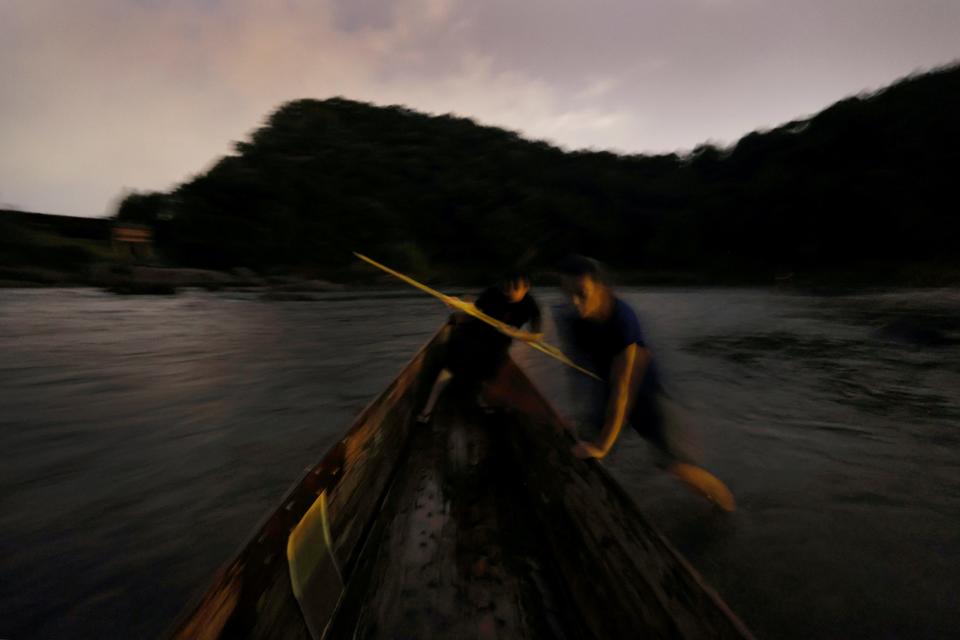 A blurred image of one man in a boat with a paddle while another man stands in water up to his ankle next to the boat to push it into place.