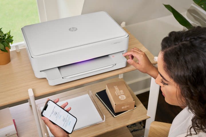 A person using an HP Envy 6020e printer with Instant Ink box in view.
