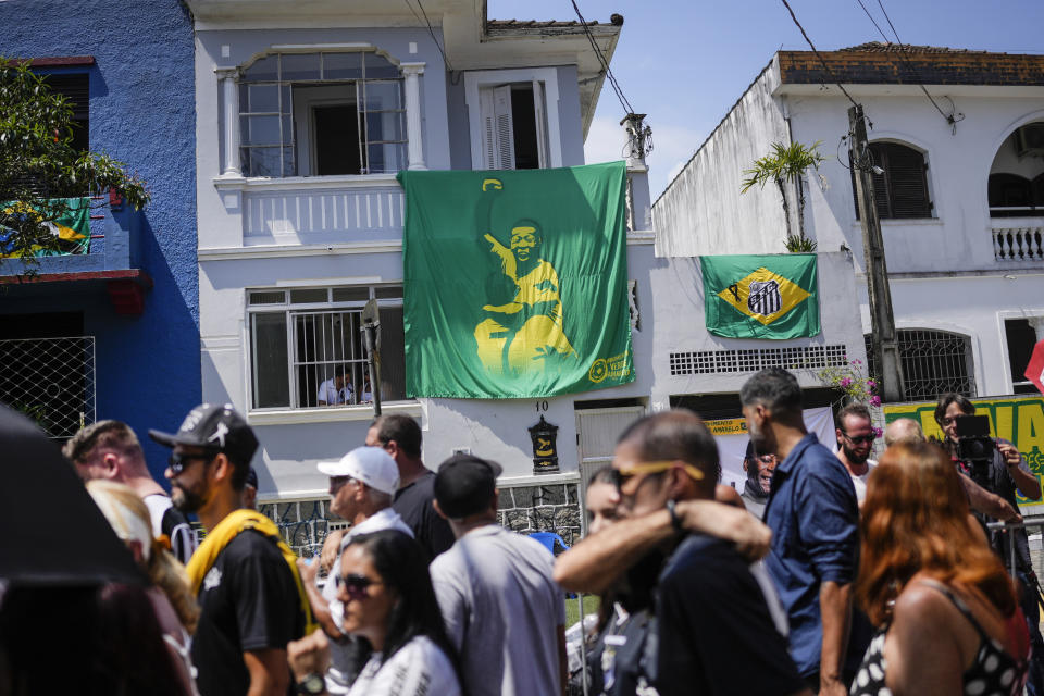 Una pancarta con la imagen de Pelé cuelga de una vivienda, detrás de la fila de gente que espera entrar al funeral en Santos, Brasil, el lunes 2 de enero de 2023 (AP Foto/Matias Delacroix)