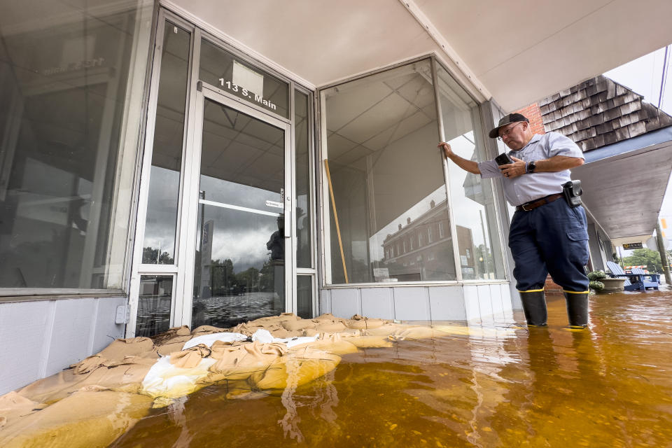 Randy Sikes speaks to his relatives on a mobile phone as he stands in residual rain water flooding the downtown area caused by Tropical Storm Debby, Thursday, Aug. 8, 2024, in Bladenboro, NC. (AP Photo/John Minchillo)