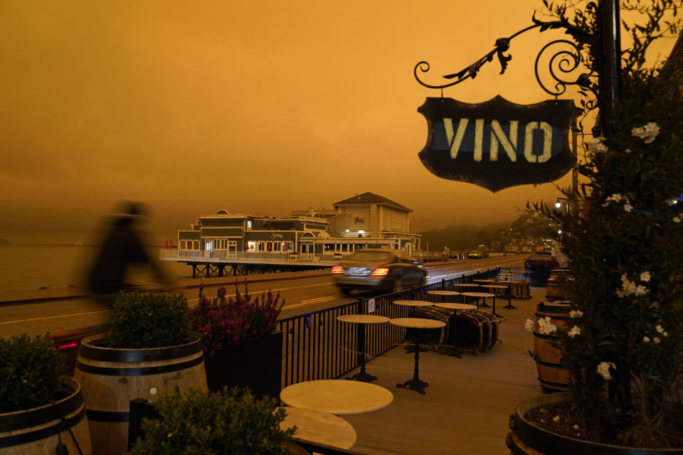 FILE - In this Sept. 9, 2020, file photo, a bicyclist rides past a seating area outside a wine bar as smoke from wildfires darken the morning sky in Sausalito, Calif. Smoke from the West Coast wildfires has tainted grapes in some of the nation’s most celebrated wine regions. The resulting ashy flavor could spell disaster for the 2020 vintage. (AP Photo/Eric Risberg, File)