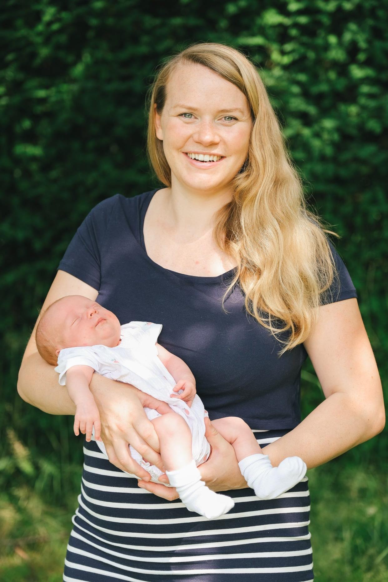 Woman standing holding baby in front of trees