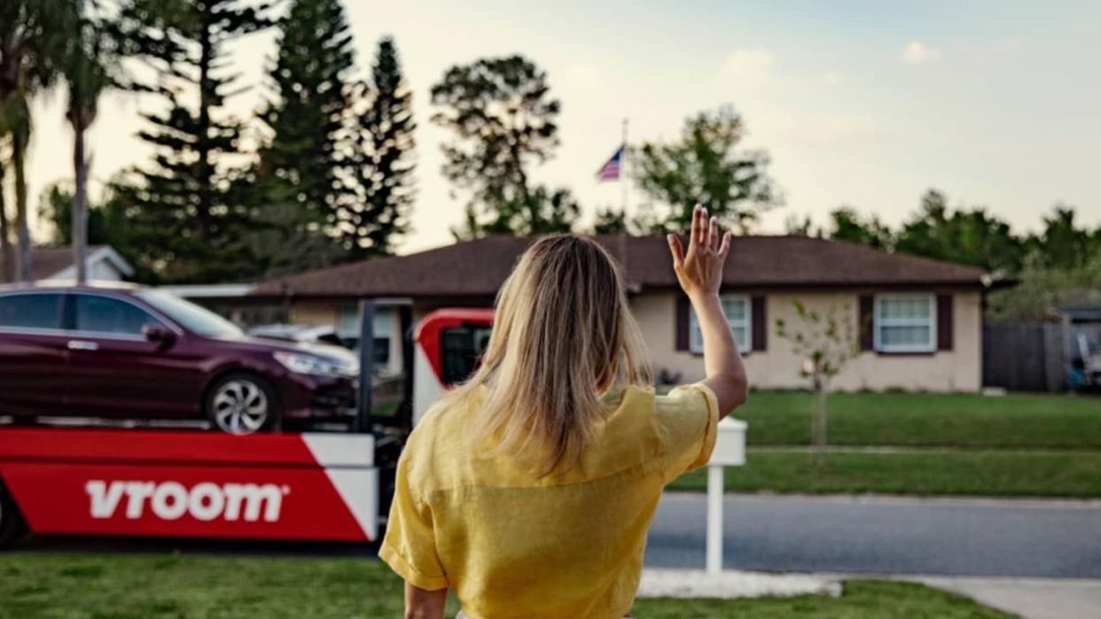 a buyer waves to a truck carrying the branding of the now discontinued car buying service vroom