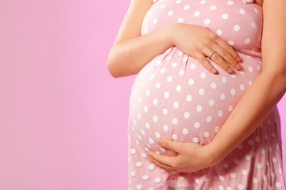 Close-up of unrecognizable pregnant woman with hands over tummy at pink background