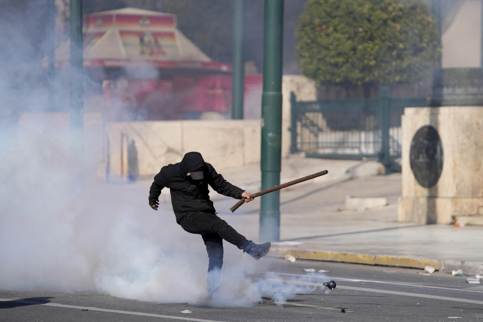 Un manifestante devuelve a patadas una granada de gas lacrimógeno a la policía durante la protesta por el desastre ferroviario, en Atenas, miércoles 8 de marzo de 2023. (AP Foto/Thanassis Stavrakis)