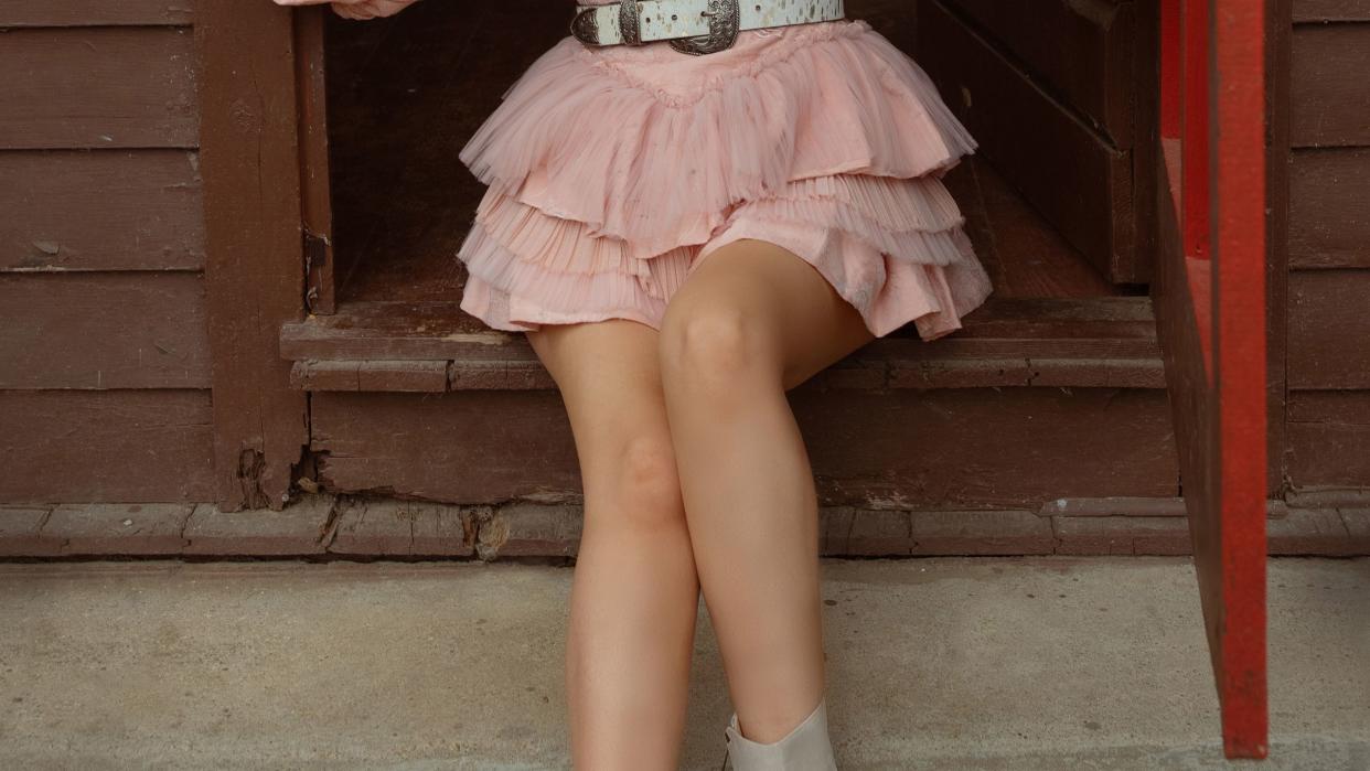 country singer songwriter mackenzie porter as an adult in pink western style dress, sitting on stoop of farmhouse