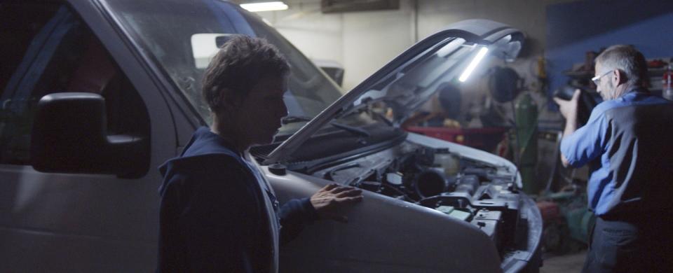 A film still shows actress Frances McDormand with her hand on a van, its hood up as a mechanic works.