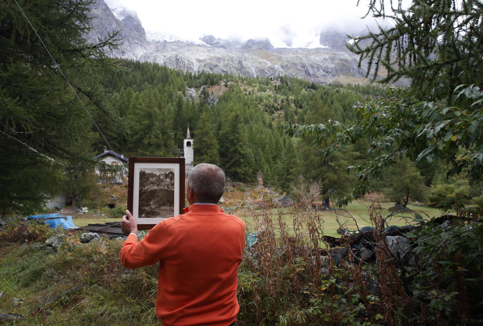 Marco Belfrond holds an old photo the Plancipieux glacier, near Courmayeur, northern Italy, Thursday, Sept. 26, 2019. Italian officials sounded an alarm Wednesday over climate change due to the threat that a fast-moving melting glacier is posing to the picturesque Val Ferret valley near the Alpine town of Courmayeur. The Planpincieux glacier, which spreads 1,327 square kilometers (512 square miles) across the Grande Jorasses peak of the Mont Blanc massif, has been moving up to 50 centimeters (nearly 20 inches) a day (AP Photo/Antonio Calanni)