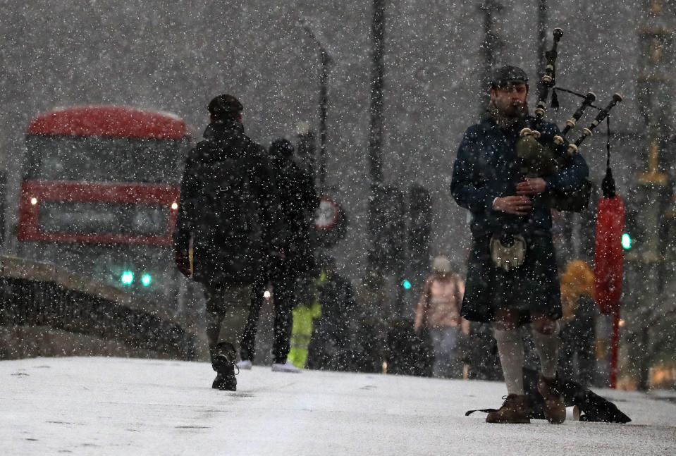 A musician play bag pipes during heavy snowfall on Westminster Bridge as temperatures dropped below freezing in London, Tuesday, Feb. 9, 2021. Snow has swept across the country, with further snowfall predicted, bringing travel problems as temperatures dropped. (AP Photo/Frank Augstein)