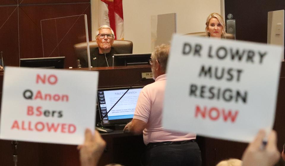 Fred Lowry listens during a Volusia County Council meeting on June 22, 2021, as audience members wave signs calling for his resignation and taking issue with conspiracy theories furthered by QAnon. Lowry's term on the County Council ends later this year and he's now running for a seat on the Volusia County School Board.