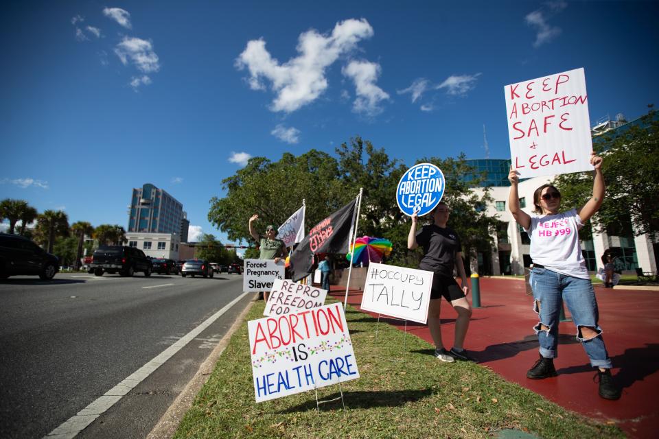 A small crowd holding signs and waving as cars pass by the Leon County Courthouse, protests Sb 300, which bans abortions after six weeks, Thursday, April 13, 2023. 