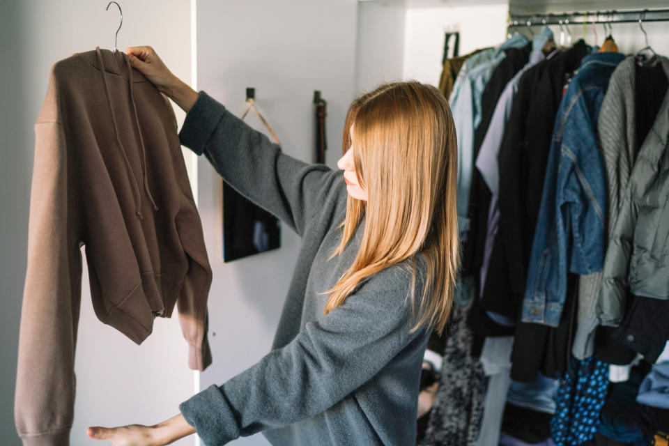 Woman examining a garment in a closet with various clothes