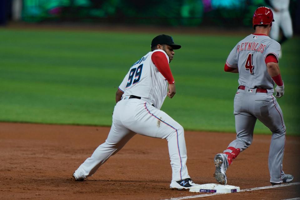 Cincinnati Reds' Matt Reynolds (4) is safe at first as Miami Marlins first baseman Jesus Aguilar (99) attempts to tag the base on time on a throwing error by starting pitcher Braxton Garrett during the first inning of a baseball game, Tuesday, Aug. 2, 2022, in Miami.