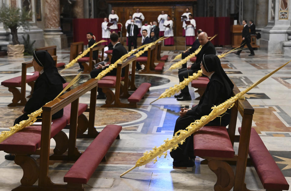 Nonnen und andere Gläubige sitzen weit auseinander neben Palmenzweigen, während sie hinter verschlossenen Türen im Petersdom auf den Beginn der päpstlichen Palmsonntagsmesse warten (Bild: Alberto Pizzoli/AFP POOL/AP/dpa)