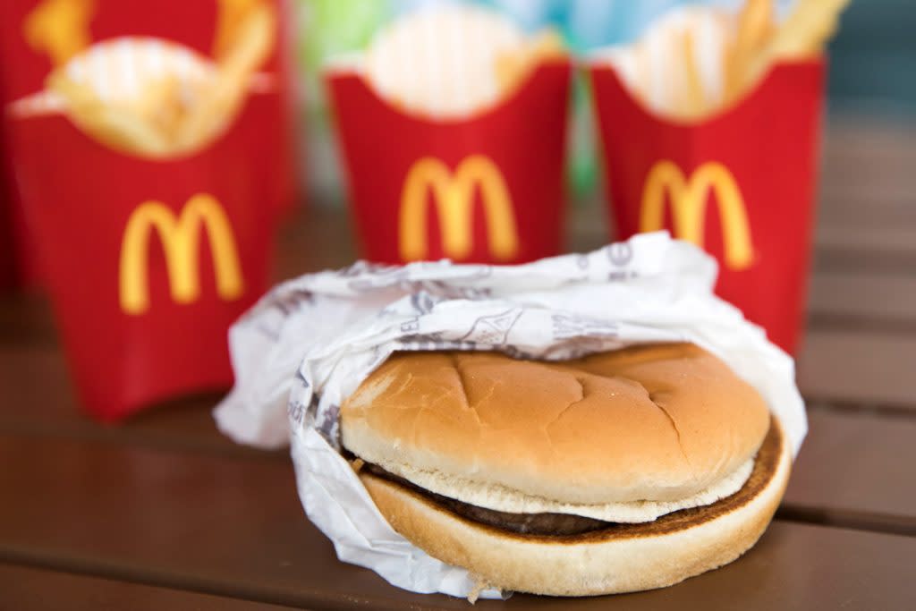 A hamburger is photographed with three orders of fries behind it. 