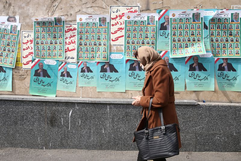 A woman walks past parliamentary election campaign posters in Tehran