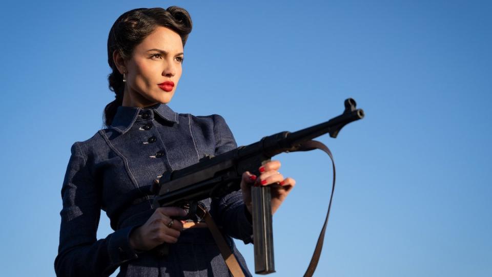 Eiza González shooting a big gun while wearing a stylish outfit outside in The Ministry of Ungentlemanly Warfare