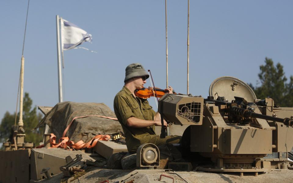 An Israeli soldier plays the violin while sitting on a military vehicle