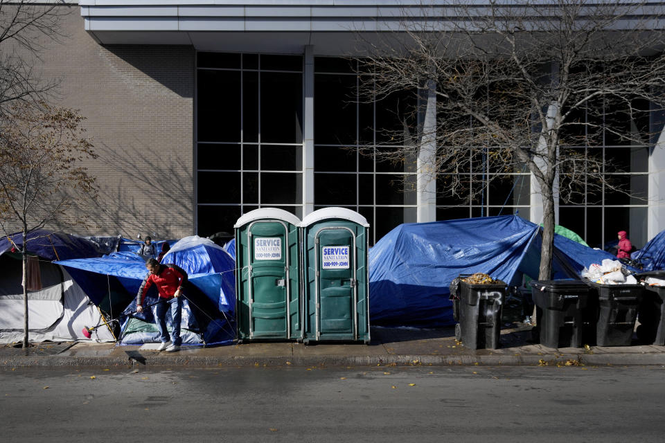 A migrant man sweeps the sidewalk of leaves and melting snow in a small tent community, Wednesday, Nov. 1, 2023, near a Northside police station in Chicago. AP Photo/Charles Rex Arbogast)