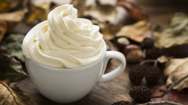 whipped cream topping a white coffee mug on wood table