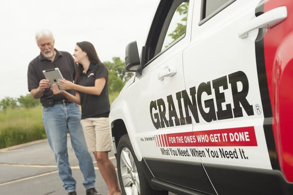 Two people standing in a parking lot next to a truck with the Grainger logo on it.