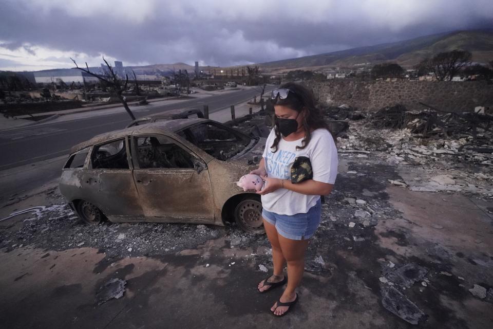 Summer Gerling picks up her piggy bank found in the rubble of her home following the wildfire Thursday, Aug. 10, 2023, in Lahaina, Hawaii. Hawaii emergency management records show no indication that warning sirens sounded before people ran for their lives from wildfires on Maui that wiped out a historic town. | Rick Bowmer, Associated Press