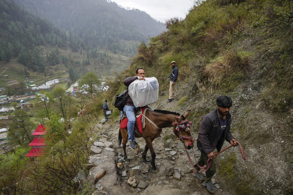 FILE- A man transports an electronic voting machine on a pony as election officials walk to a polling booth in a remote mountain area on the eve of the first round of voting at Dessa village in Doda district, Jammu and Kashmir, India, April 18, 2024. (AP Photo/Channi Anand)