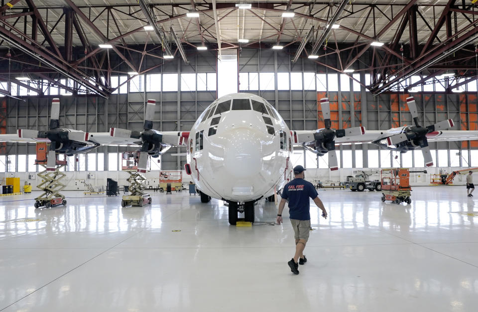 Aircraft Mechanic Cody Poole walks past one of the recently acquired C-130 aircraft, that will be used for firefighting, hangared at the California Department of Forestry and Fire Protection's Sacramento Aviation Management Unit based at McClellan Airpark in Sacramento, Calif., Friday, July 23, 2021. Firefighters are trying to become smarter in how they prepare for the drought- and wind-driven wildfires that have become more dangerous across the American West in recent years, including by adding aircraft like the Sikorsky Firehawk helicopters or military surplus C-130 transport aircraft retrofitted to drop fire retardant. (AP Photo/Rich Pedroncelli)