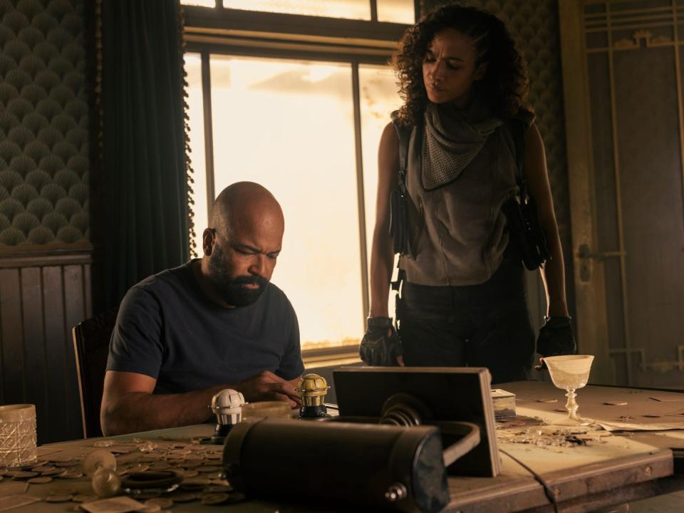 A scene from "Westworld" season four showing a man sitting at a desk with a woman looking over his shoulder.